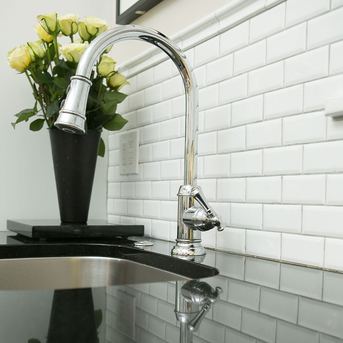 subway tile backsplash behind modern chrome faucet on black marble countertops in renovated kitchen